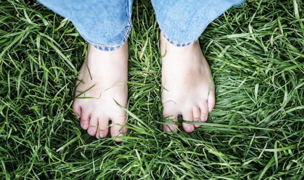 Bare feet standing in fresh green grass, representing grounding, connection to the earth, mindfulness, and presence